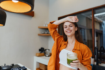 Canvas Print - Happy young woman enjoying a healthy green smoothie at home in a stylish kitchen, showcasing wellness and vibrant lifestyle choices