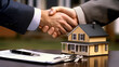 © MuhammadYasir - A handshake signifies a real estate deal with a toy house contract pen and keys nearby