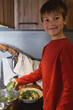 © Marc Elias - Smiling boy cooking in the kitchen while holding a piece of broccoli.