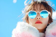 © Artsby - Woman in pink fur coat and blue sunglasses against blue sky.