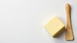 © vattana - A block of pale yellow dairy product and a small wooden spreader on a white background