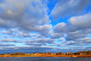 Wall Mural - River bank. Cloudy sky. Village on the river bank.