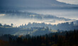 © anatoliy_gleb - Morning sunlight streams through mist, illuminating serene mountain village nestled among forested hills. Light creates ethereal rays that gently touch autumn foliage and houses scattered on slopes.