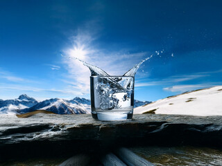 Aufkleber - A glass of water splashes dramatically against a backdrop of snow-capped mountains and a bright sun.  Pure refreshment in a pristine setting.