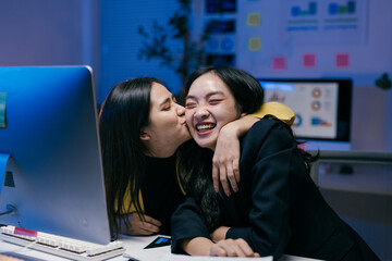 Wall Mural - Two young businesswomen are hugging and kissing in the office, celebrating their success after closing a deal late at night