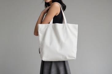 Young woman holding a plain canvas tote bag, ideal for mockup design templates, isolated against a neutral gray background.