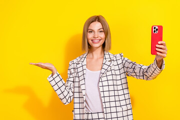 Confident young businesswoman taking selfie against vibrant yellow background wearing stylish checked suit and white jacket