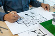 © Kield KD - A man is holding a model of a house on a table with other drawings and blueprints. Scene is focused and professional, as the man is likely an architect or engineer working on a project