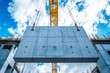 © Lubos Chlubny - Crane lifting concrete slab at construction site on cloudy day