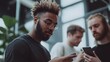 © Aditya - A young man with dreadlocks and glasses is focused on his phone, while two others in the background are also using their phones. The image suggests a social and connected atmosphere.