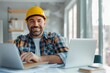 © Vilaysack - A smiling construction worker in a hard hat sits at a desk with laptops and documents, blending traditional and modern work environments.
