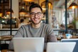 © Vilaysack - A smiling man with glasses works on two laptops in a cozy cafe setting, showcasing a blend of productivity and relaxed ambiance.