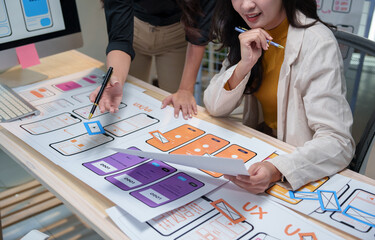 Two female web designers collaborating on ux design for a mobile application during a meeting, analyzing layouts and functionalities while brainstorming innovative solutions