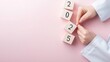 © sakon - Hands adjusting wooden blocks with year numbers on a pink background, symbolizing a change or transition