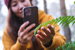 © Farknot Architect - A woman taking photos of green plant with smartphone in the forest