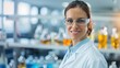 © Vilaysack - A smiling woman in a lab coat and safety glasses stands in a laboratory filled with colorful glassware, showcasing a professional and scientific environment.