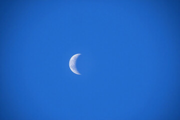 crescent moon against clear blue sky showing surface texture