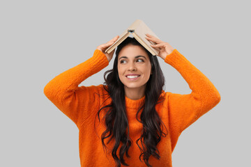 Portrait of funny young woman with book on grey background