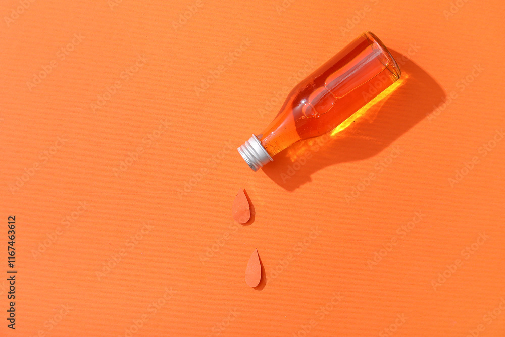 Composition with bottle of essential oil and paper drops on orange background