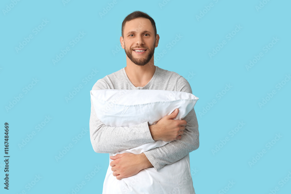 Young man in pajamas with soft pillow on blue background. World Sleep Day