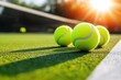 © Tondone - Several tennis balls on a vibrant green court bask under the warm glow of the sun. Perfect for sports-related content or tennis-themed designs.