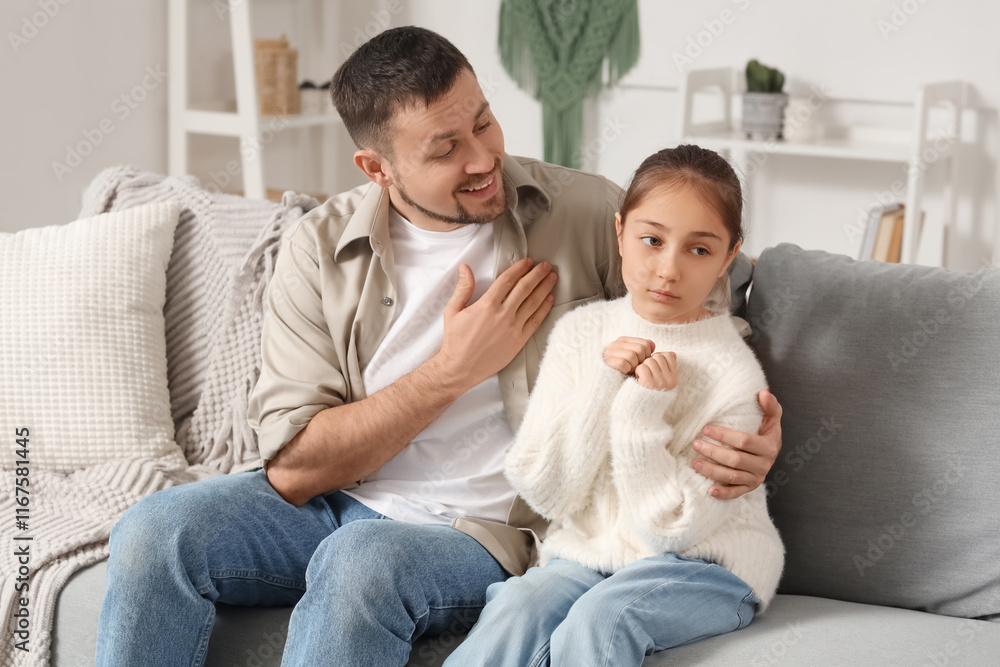 Apologetic father hugging his daughter on sofa at home