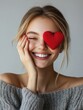 © Johannes - valentine's day, beauty and people concept - happy smiling beautiful young woman covering one eye by red heart over grey background
