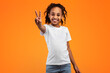 © Prostock-studio - Celebrating Success. Portrait of young African American girl with curly hair wearing casual t-shirt standing and showing two fingers doing victory v sign, looking to the camera. Number 2