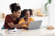 © Prostock-studio - Creative black mother and daughter working on school project, using modern laptop, taking notes, cheerful afro-american woman helping her teen kid with homework, kitchen table, copy space