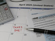 © KilmerMedia - A 2025 calendar noting the April 15 USA Internal Revenue Service IRS income filing deadline for year 2024 taxes is shown up close, with a calculator, ink pen, and glasses in the frame.