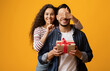 © Prostock-studio - Loving Young Woman Covering Boyfriend's Eyes And Surprising Him With Gift, Cheerful Middle Eastern Lady Showing Shh Sign, Greeting Her Husband With Birthday Or Valentines Day Over Yellow Background