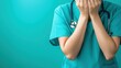 © Thanawat - A healthcare professional in scrubs covers their face with their hands, expressing distress or exhaustion against a teal background.