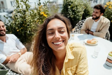 Happy young woman smiling with closed eyes during a lunch with friends on a rooftop terrace, enjoying summer and friendship