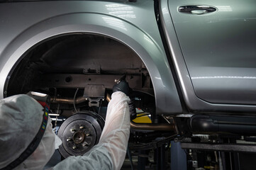 An auto mechanic applies anti-corrosion mastic to the underbody of a car.