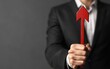 © Wan - A businessman holds a red arrow symbolizing upward growth and progress against a dark background, conveying a message of success and motivation.
