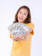 © suphaporn - Cheerful and Beautiful Asian Woman Holding Dollar Bills with a Big Smile, Isolated on White Background, Representing Wealth, Financial Success, Happiness, and Confidence in Modern Lifestyle Concepts