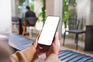 Wall Mural - mockup image of a woman holding and using mobile phone with blank desktop in cafe