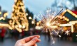© Wimon - A hand holds a sparkling sparkler in front of festive holiday lights and a decorated tree, creating a magical, celebratory atmosphere.