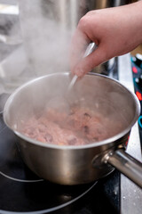 Wall Mural - A hand stirs a pot of steaming risotto on a stovetop. The creamy rice dish has hints of pink and is surrounded by rising steam, indicating a warm, inviting cooking scene.