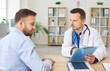© Studio Romantic - Portrait of a young man patient in medical office listening to a friendly male doctor holding report file with appointment and giving consultation during medical examination in clinic.
