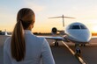 © Milos - A professional woman in a white suit stands overlooking a private jet at sunset, symbolizing success and adventure in a luxurious travel environment.