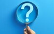 © PHOTOS  STORY - Hand holding a magnifying glass over question marks on a blue background, focusing on one question mark while others are blurred, symbolizing inquiry and curiosity