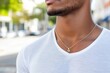 © Milos - A close-up of a minimalist gold pendant necklace worn by a man in a simple white shirt, adding a touch of elegance and sophistication to his casual look.
