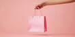 © Orod - Minimalist scene with a hand holding a pink shopping bag against a pastel pink background