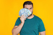 © Volodymyr - Business man in t-shirt with cash money dollars banknotes isolated on yellow studio background. Hundred dollar bill, financial concept.