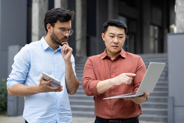 Wall Mural - Two office workers discussing a work project outside an office building, miscellaneous business meeting of office company workers, discussing looking at a laptop, serious and focused.