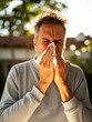 © Karat - A man outdoors experiencing seasonal allergies or a cold, sneezing into a tissue.