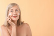 © New Africa - Senior woman applying face cream on beige background. Space for text
