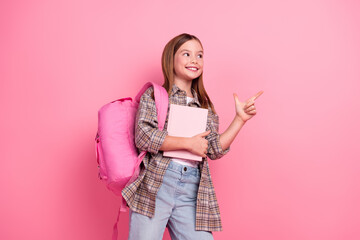 Wall Mural - Smiling girl in casual outfit pointing to the side with a cheerful expression standing against a pink background