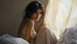 © imran - Young woman in a beige slip dress, her dark hair cascading, sitting serenely on a bed with direct eye contact